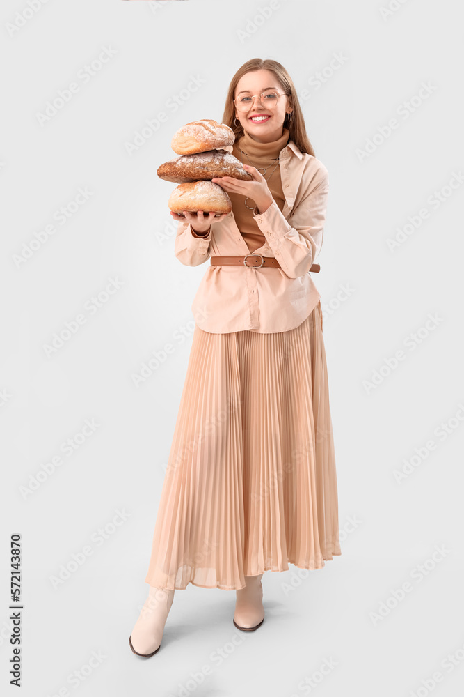 Young woman with loaves of fresh bread on light background