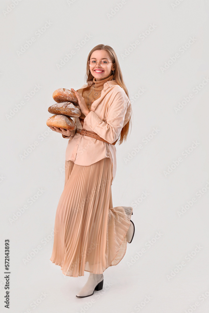 Young woman with loaves of fresh bread on light background