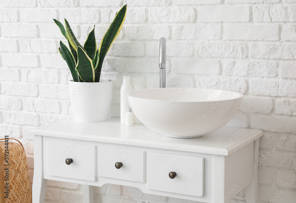 Table with sink, bath accessories and houseplant near white brick wall