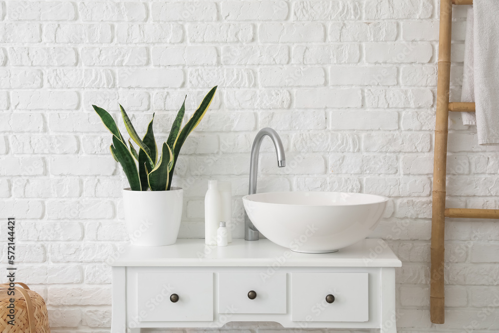 Table with sink, bath accessories and houseplant near white brick wall