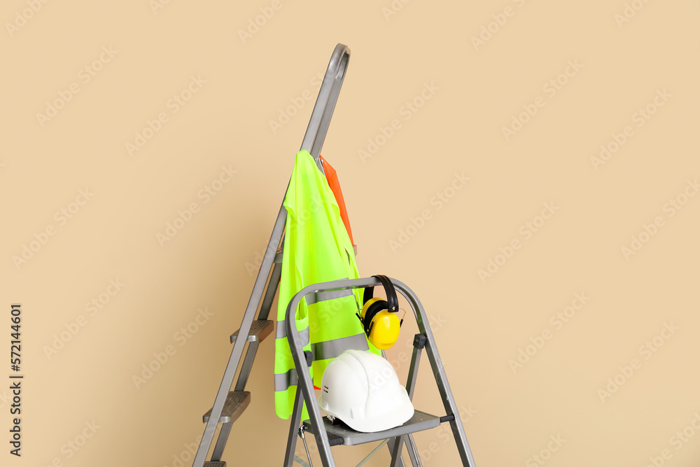 Stepladders with builders equipment and reflective vests near beige wall