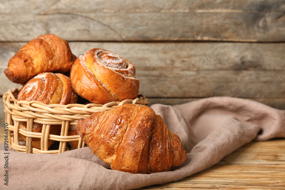 Basket with delicious croissants and cinnamon rolls on napkin near wooden wall