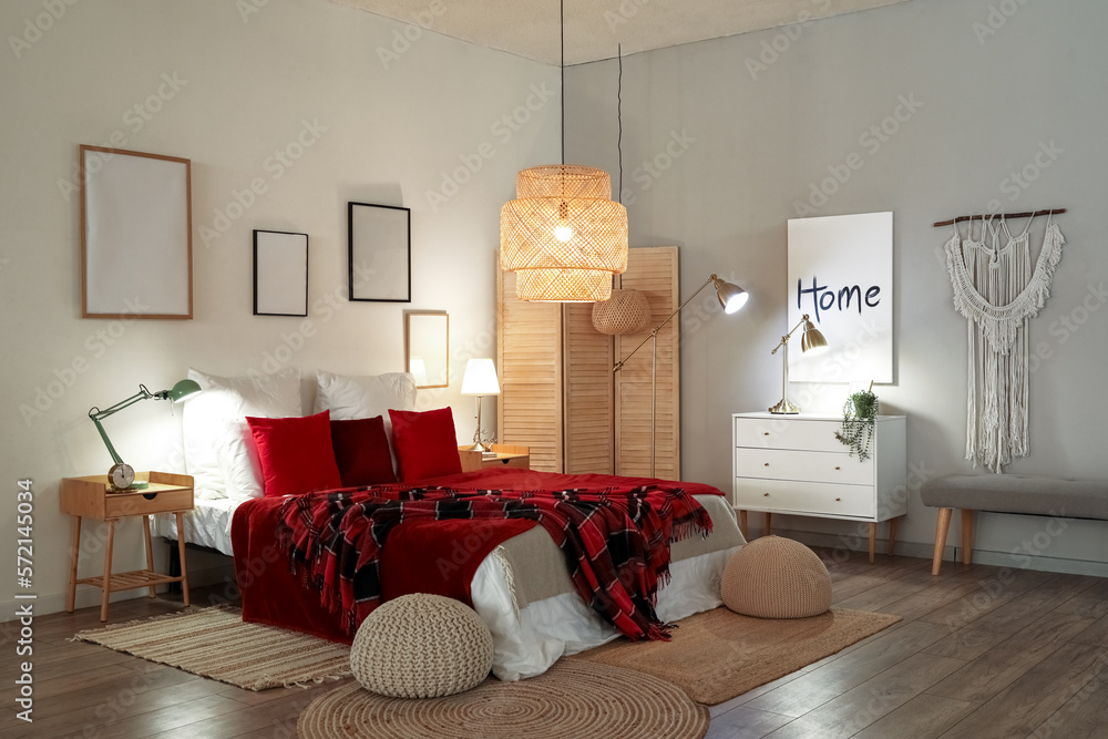 Interior of bedroom with red checkered blankets on bed and glowing lamps late in evening