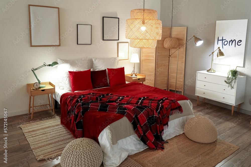 Interior of bedroom with red checkered blankets on bed and glowing lamps late in evening