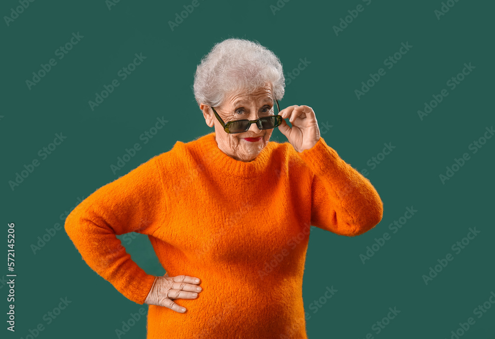 Senior woman in sunglasses and orange sweater on green background