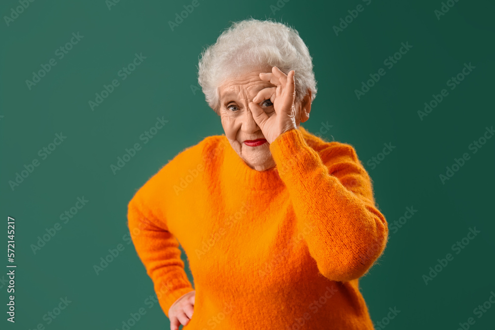 Senior woman in orange sweater showing OK on green background