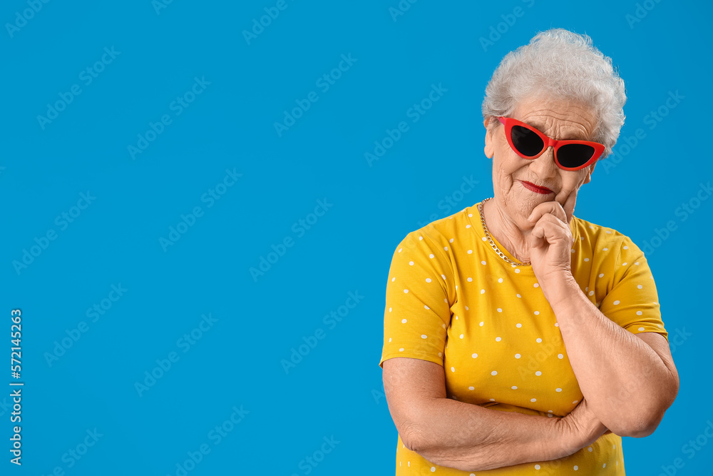 Senior woman in stylish sunglasses on blue background