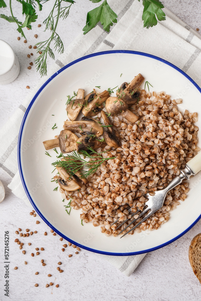 Plate of tasty buckwheat porridge with mushrooms and dill on grey table