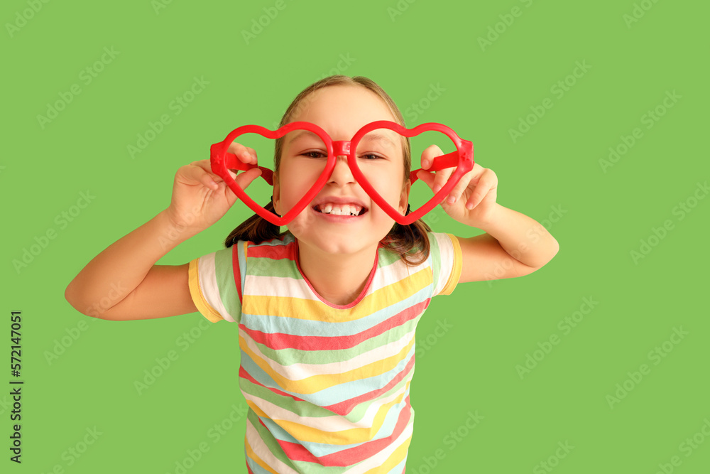 Little girl in funny eyeglasses on green background. April Fools Day celebration