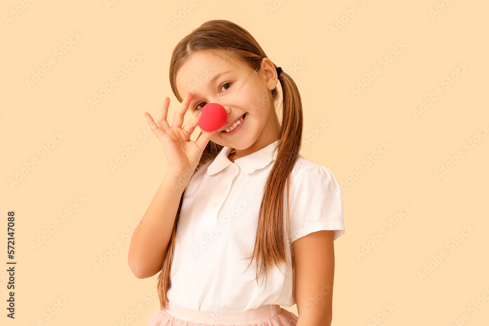 Little girl with clown nose on beige background. April Fools Day celebration