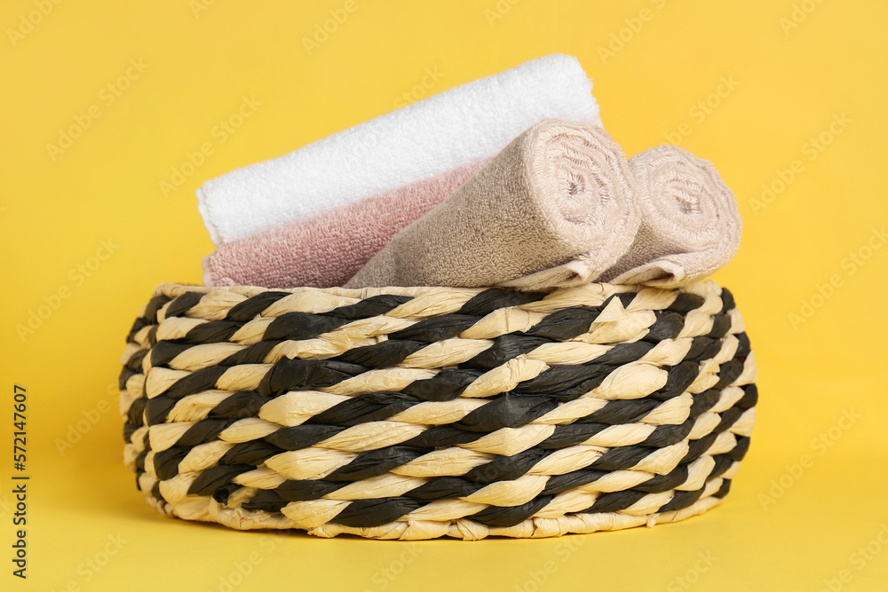 Basket with clean towels on yellow background