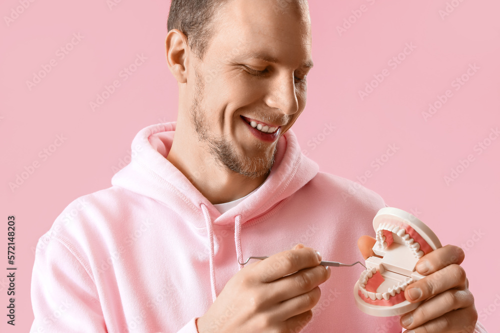 Young bearded man with jaw model and dental tool on pink background, closeup