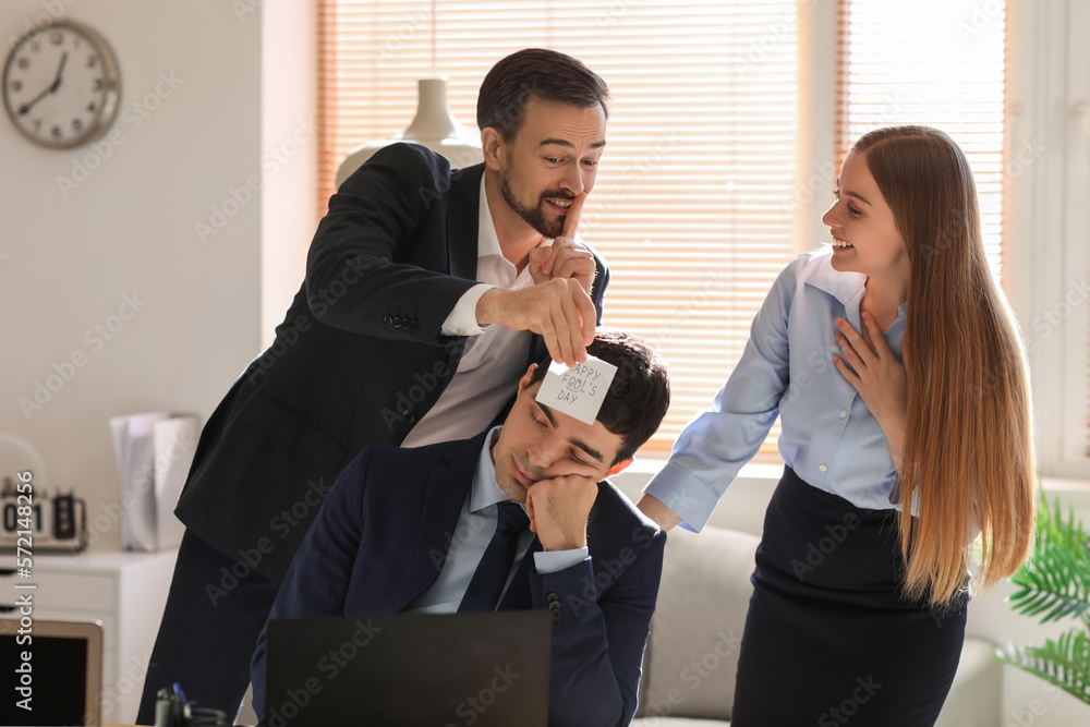 Young man and woman playing a prank on their sleeping colleague in office. April Fools Day celebrat