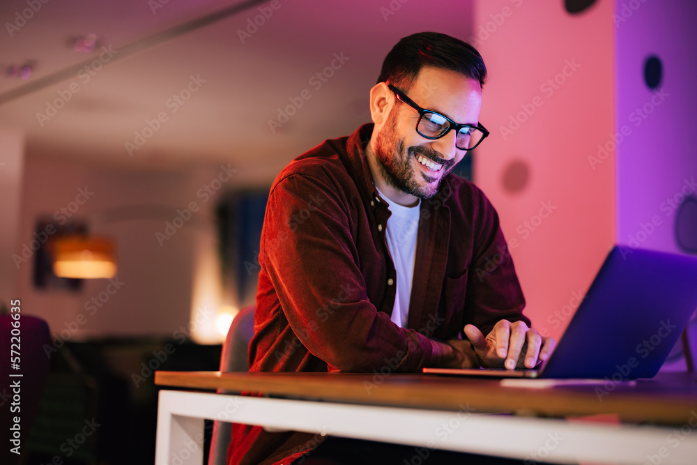 Smiling man talking online with colleagues, using a laptop.