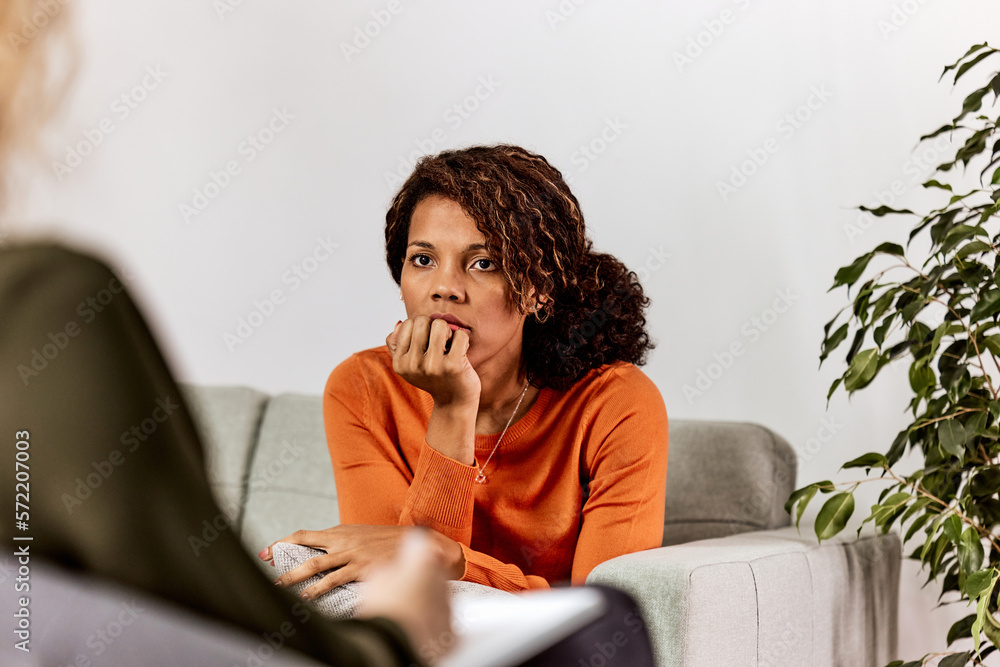 Psychologist with notebook talking to stressed  African woman patient at psychotherapy session.