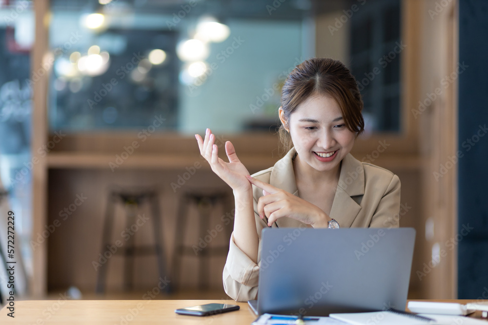 Businesswoman working on laptop in office gestures to greet colleagues via video conferencing using 