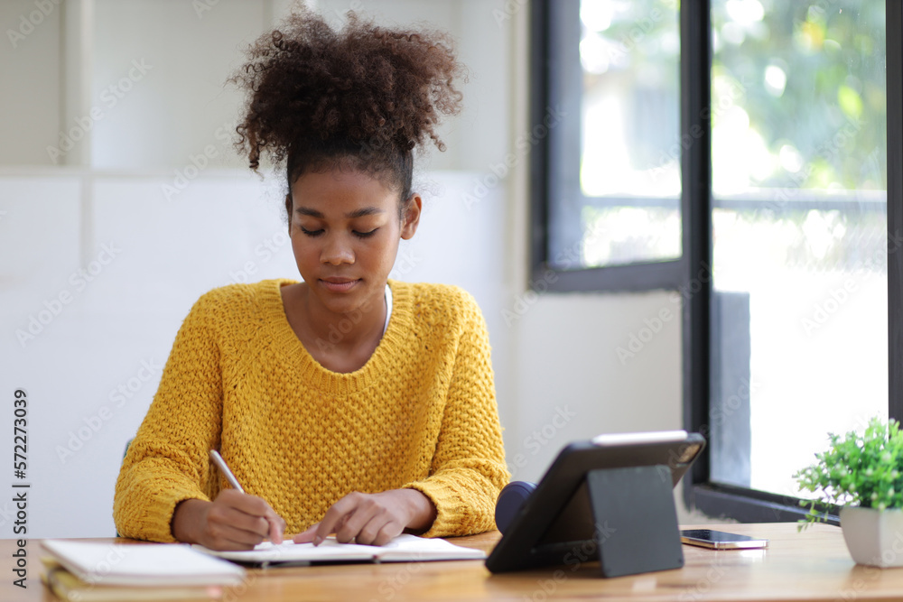 Young african woman working with tablet and reading books preparing for exams at her home.