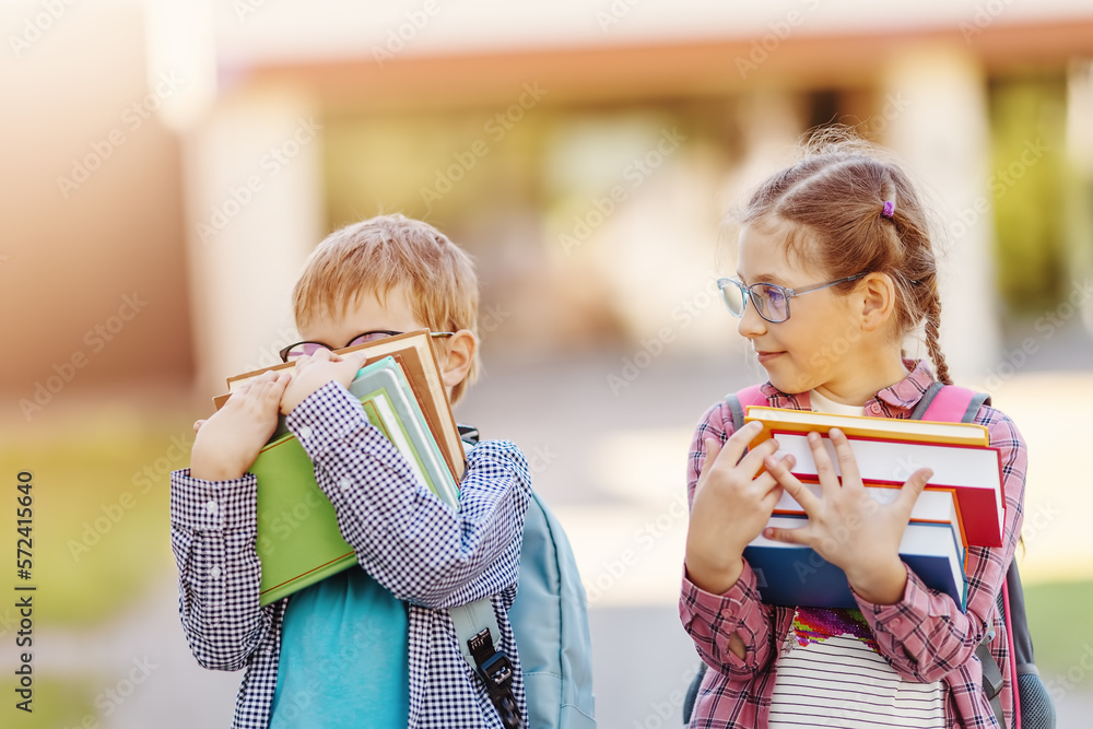 Girl and boy in glasses standing with books in their hands.