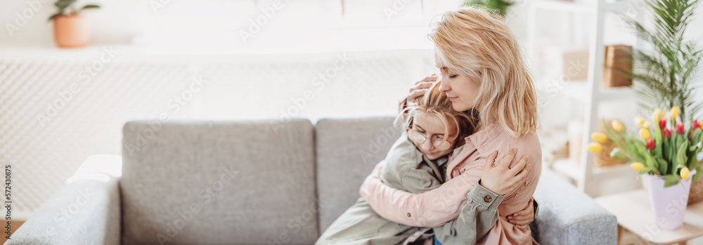 Mother and daughter sitting on the sofa indoor and embracing.