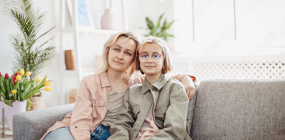 Mother and daughter sitting on the sofa indoor and embracing.