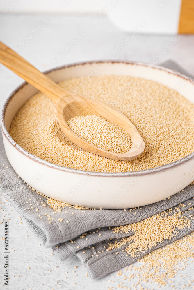 Bowl and spoon of amaranth seeds on light background, closeup