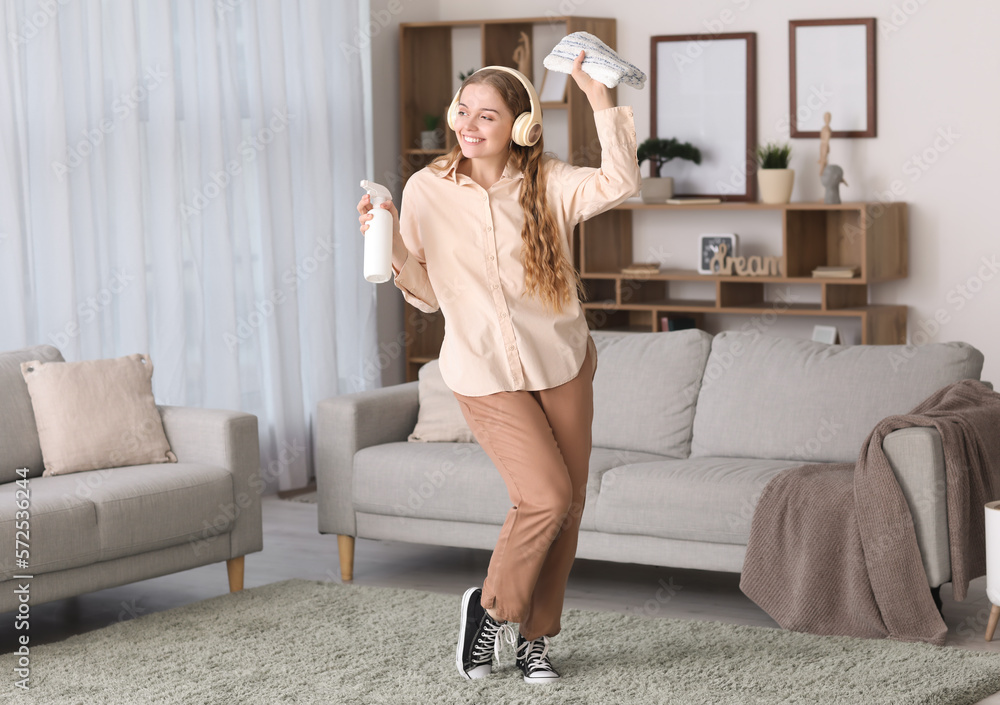 Young woman in headphones with rag and detergent dancing at home