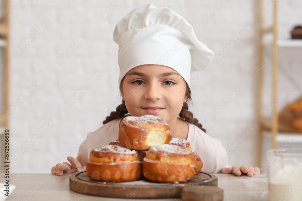 Little baker and tasty buns on table in kitchen, closeup