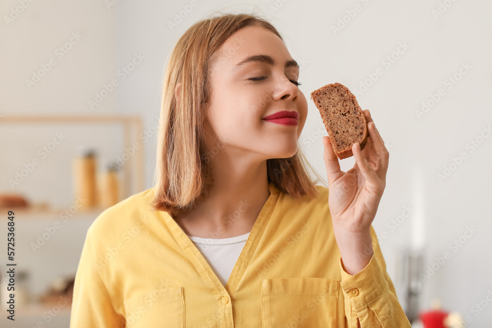 Young woman with slice of fresh bread in kitchen, closeup