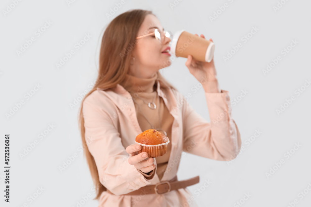 Young woman with tasty cupcake drinking coffee on light background