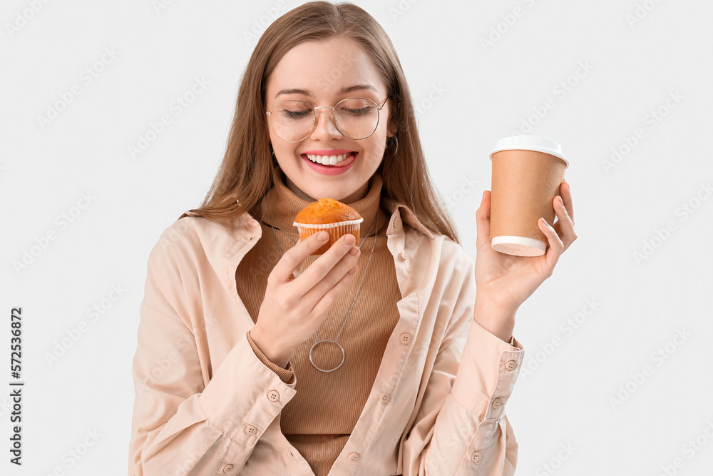 Young woman with tasty cupcake and cup of coffee on light background, closeup