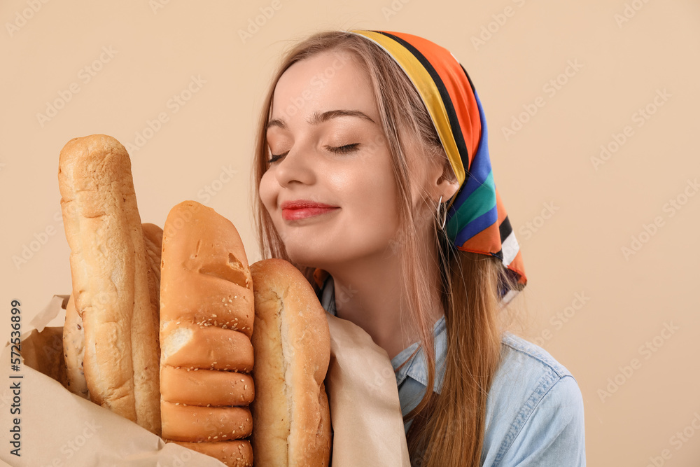 Young woman with fresh baguettes on beige background, closeup