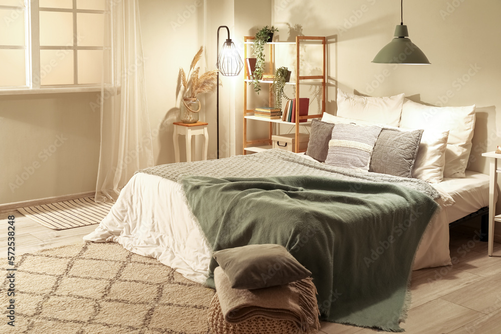 Interior of bedroom with green blankets on bed and glowing lamps late in evening