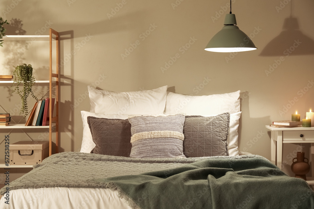 Interior of bedroom with green blankets on bed, burning candles and glowing lamps late in evening