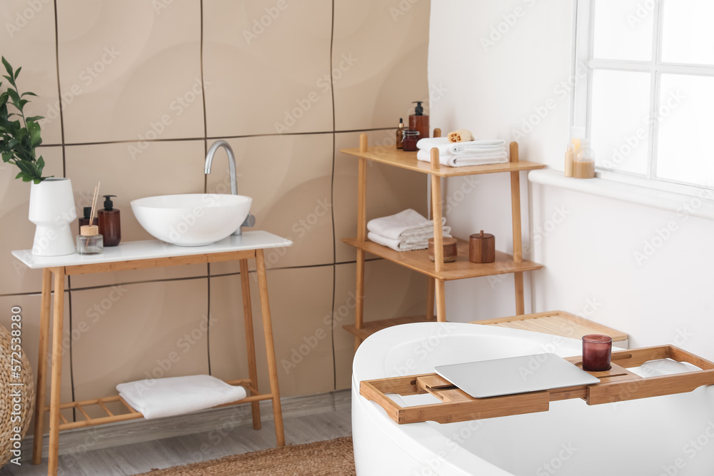 Interior of bathroom with modern bathtub, ceramic sink and laptop on board