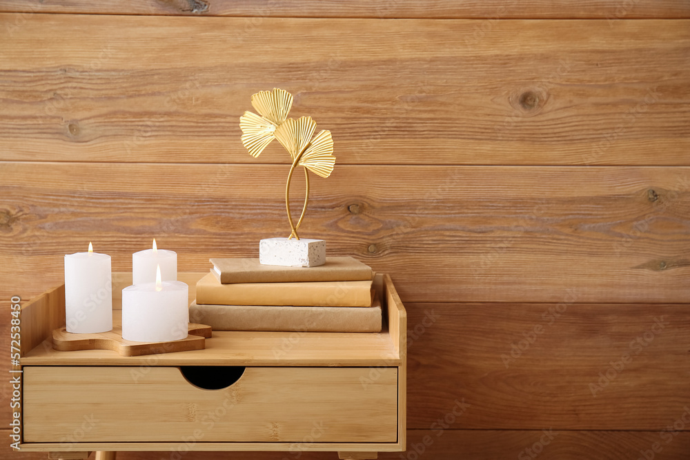 Burning candles with books and decor on table near wooden wall