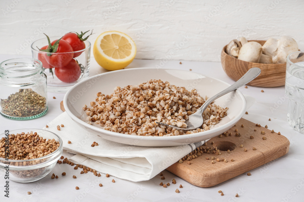 Board with plate of tasty buckwheat porridge on white table