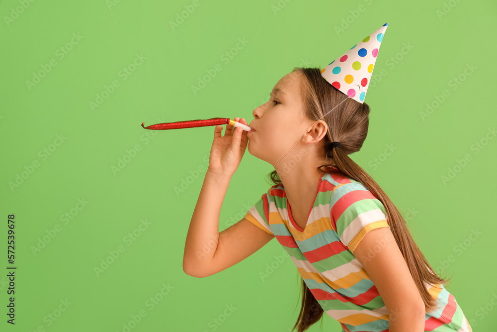 Little girl in party hat with blower on green background. April Fools Day celebration