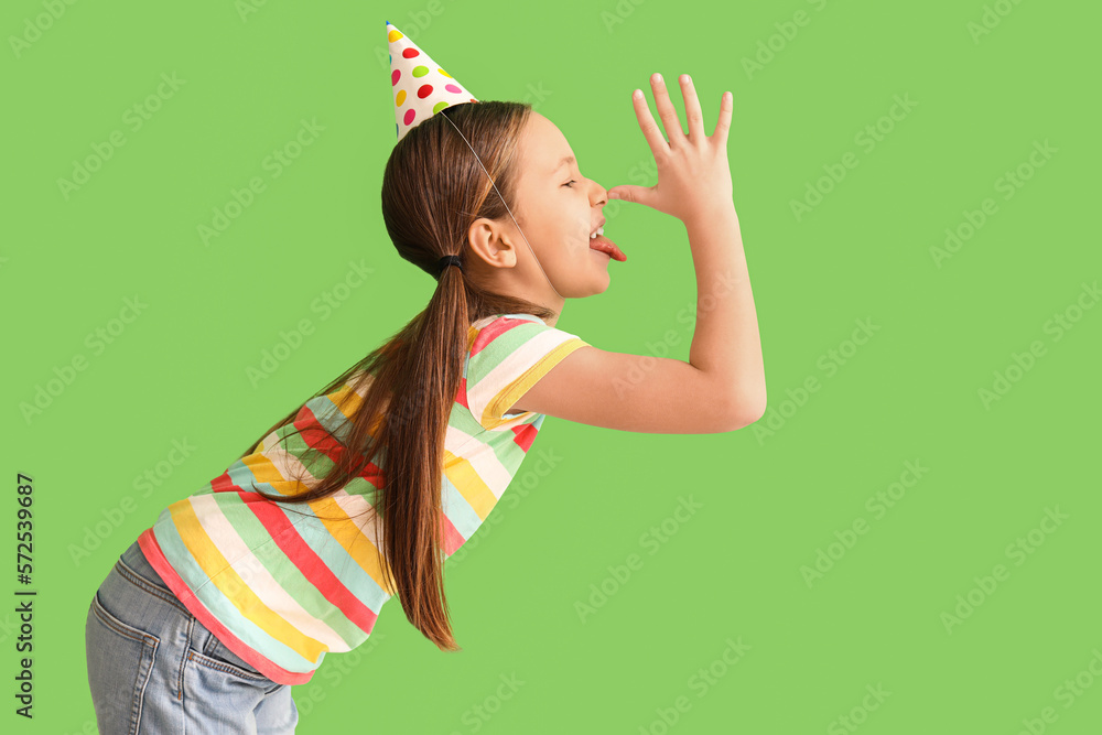 Funny little girl in party hat on green background. April Fools Day celebration