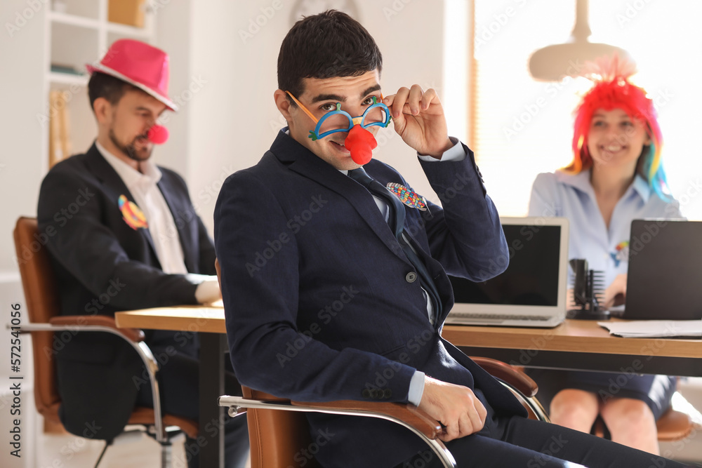 Young man with funny disguise working in office. April Fools Day celebration