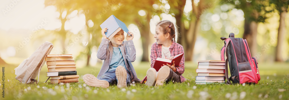 Boy and girl sitting on the meadow with books in their hands.