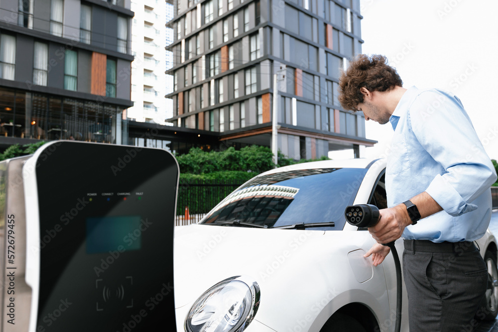 Progressive businessman insert charger plug from charging station to his electric vehicle with apart