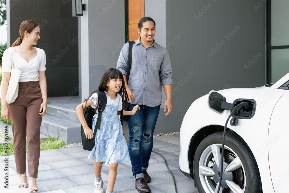 Progressive young parents and daughter with electric vehicle and home charging station. Green and cl