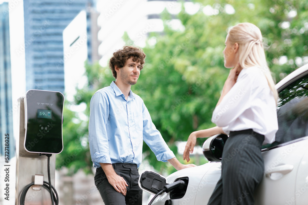 Progressive businessman and businesswoman with electric car parking and connected to public charging