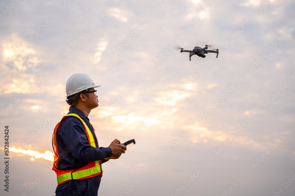 Asian surveyors or explorer use drones to view construction sites or check security at sunset.