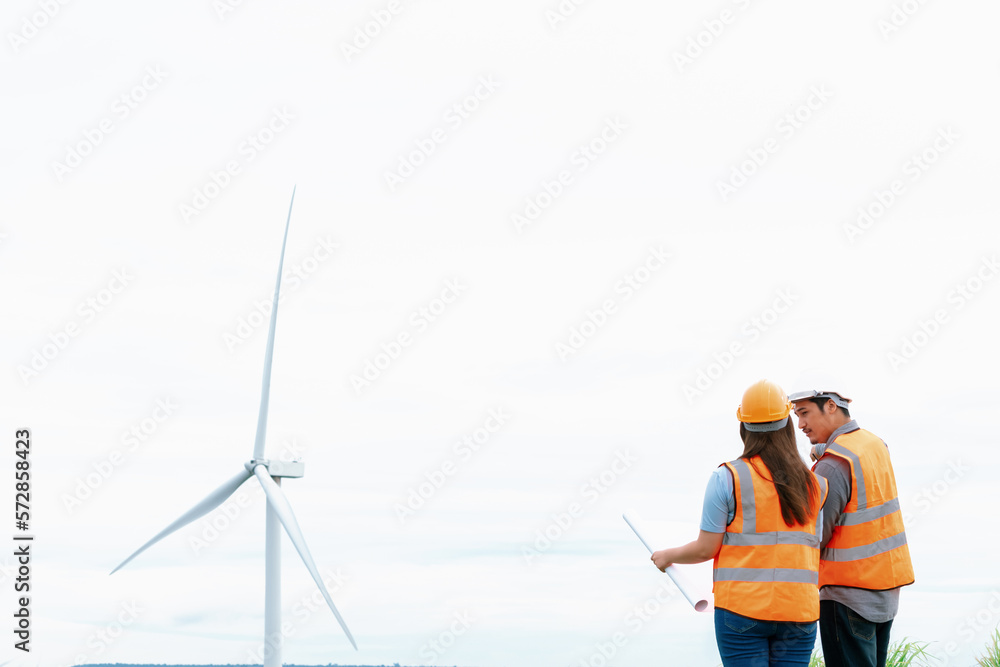 Male and female engineers working on a wind farm atop a hill or mountain in the rural. Progressive i