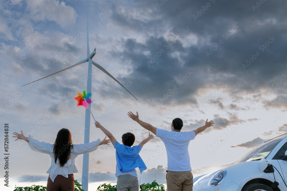 Concept of progressive happy family enjoying their time at wind farm with electric vehicle. Electric