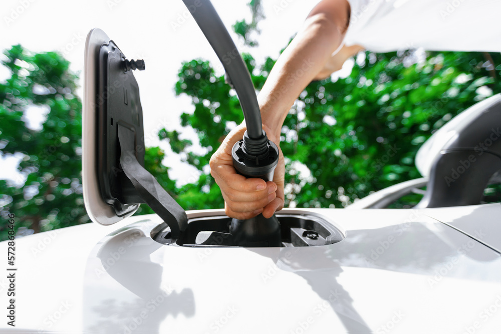 Focus below view image of hand insert EV charger plug into electric vehicle from below view with blu