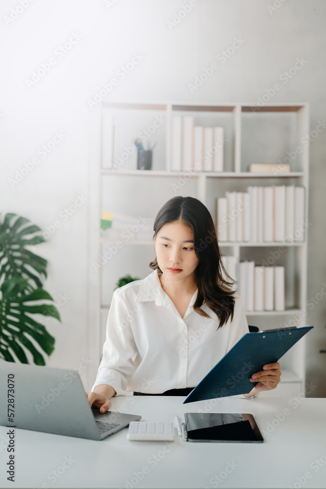 Young beautiful woman using laptop and tablet while sitting at her working place. Concentrated at wo