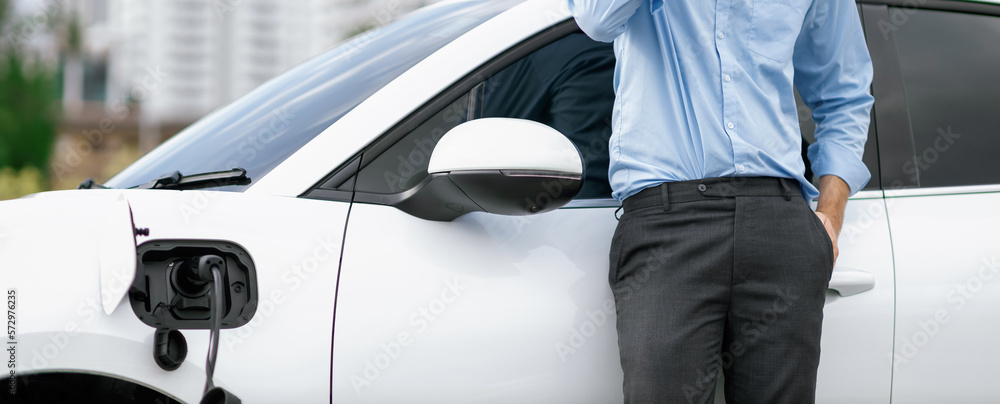 Closeup progressive suit-clad businessman with his electric vehicle recharge his car on public charg