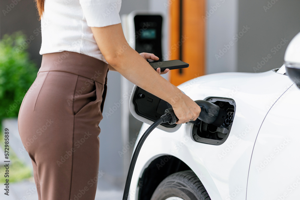 Closeup progressive woman install cable plug to her electric car with home charging station. Concept